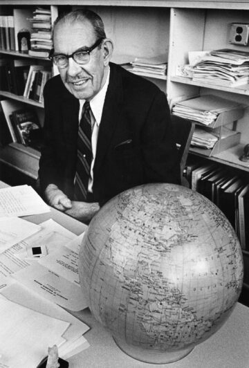 Grayscale portrait of Arthur Robinson sitting at desk beside model of earth.
